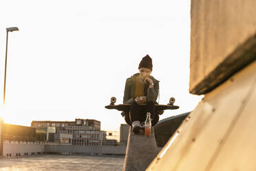 Stylische junge Frau mit Skateboard und Handy auf einem Parkdeck - UUF18338
