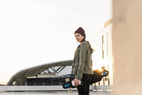 Stylische junge Frau mit Skateboard auf Parkdeck - UUF18340