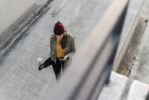 Stylish young woman with skateboard and cell phone on parking deck - UUF18342