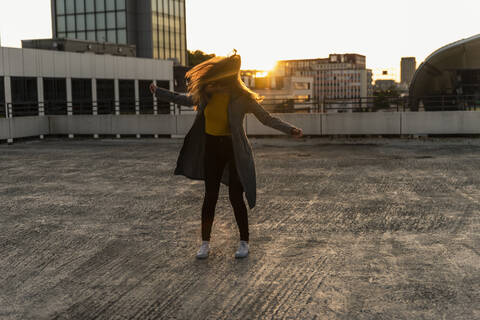 Fröhliche junge Frau tanzt auf einem Parkdeck bei Sonnenuntergang, lizenzfreies Stockfoto