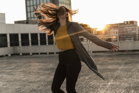 Fröhliche junge Frau tanzt auf einem Parkdeck bei Sonnenuntergang, lizenzfreies Stockfoto