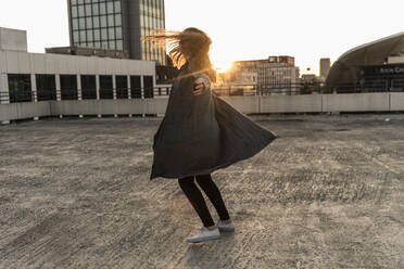 Fröhliche junge Frau tanzt auf einem Parkdeck bei Sonnenuntergang - UUF18347