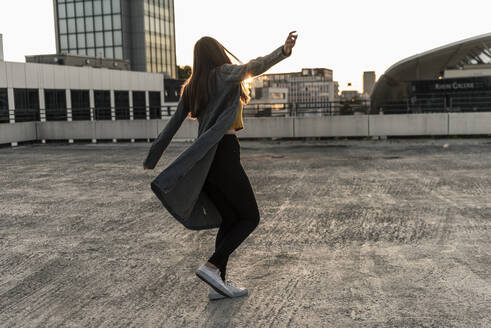 Fröhliche junge Frau tanzt auf einem Parkdeck bei Sonnenuntergang - UUF18348