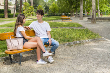 Junges Paar, das in einem Park auf einer Bank sitzt und miteinander spricht - MGIF00622