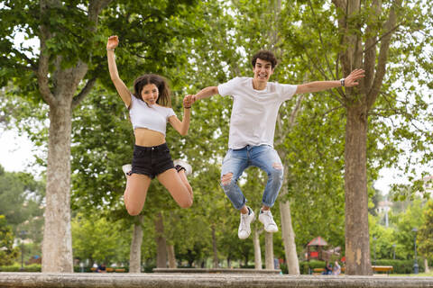 Junges Paar springt von einer Mauer im Park, lizenzfreies Stockfoto