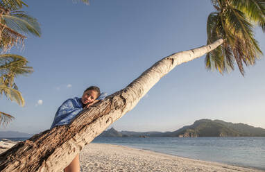 Asian woman on palm tree on beach - BLEF12011