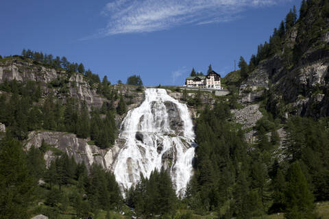 Gebäude über einem Wasserfall an einem abgelegenen Berghang, lizenzfreies Stockfoto
