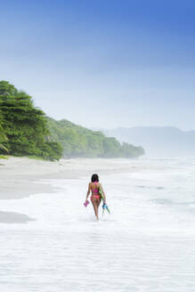 Hispanic woman carrying fins on beach - BLEF12072