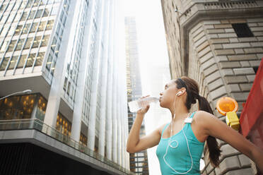 Hispanic woman drinking water bottle under highrise buildings - BLEF12081