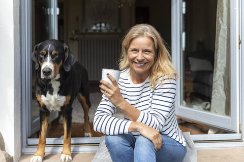 Porträt einer glücklichen reifen Frau, die mit einer Kaffeetasse auf einer Terrasse sitzt, lizenzfreies Stockfoto