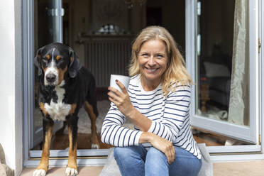 Porträt einer glücklichen reifen Frau, die mit einer Kaffeetasse auf einer Terrasse sitzt - FMKF05760