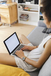 Junge Frau benutzt ihren Laptop auf dem Sofa - MRAF00409