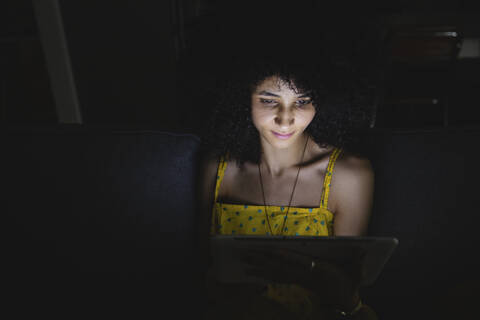 Junge Frau benutzt ihr digitales Tablet in der Nacht auf dem Sofa, lizenzfreies Stockfoto