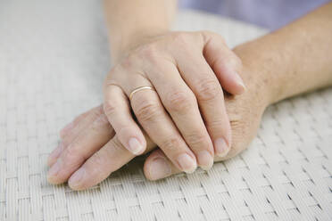 Senior couple sitting at garden table holding hands, close-up - AHSF00690