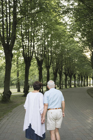 Rückansicht eines älteren Paares, das Hand in Hand in einem Park spazieren geht, lizenzfreies Stockfoto