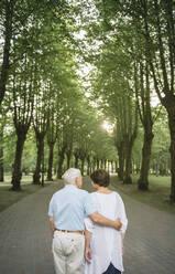 Rückansicht eines älteren Paares, das bei Sonnenuntergang in einem Park spazieren geht - AHSF00694