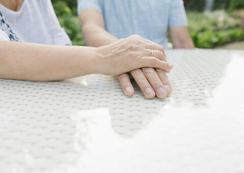 Älteres Paar sitzt am Gartentisch und hält sich an den Händen, Nahaufnahme, lizenzfreies Stockfoto