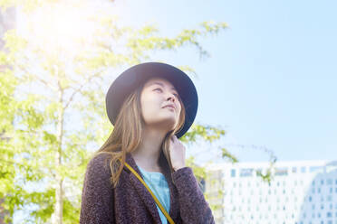 Barcelona, Spain. Asian girl with hat looking away with confidence while dreaming outdoors - GEMF02994