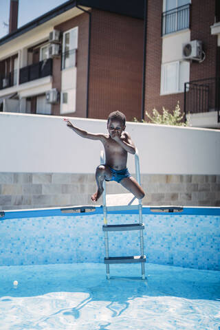 Glücklicher kleiner Junge auf einer Leiter im Schwimmbad, lizenzfreies Stockfoto