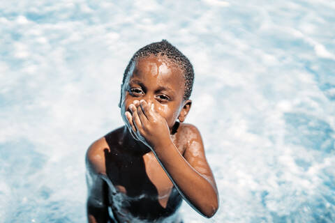 African child having fun in swimming pool, holding nose stock photo