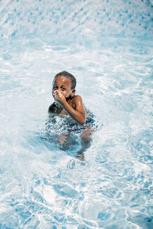 Afrikanisches Kind hat Spaß im Schwimmbad und hält sich die Nase zu - OCMF00529