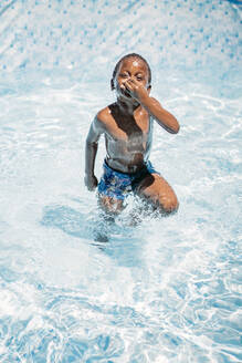 Afrikanisches Kind hat Spaß im Schwimmbad und hält sich die Nase zu - OCMF00530