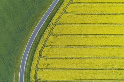 Abstrakte Luftaufnahme einer Landstraße durch landwirtschaftliche Felder mit Rapsfeld und grünem Weizenfeld, Franken, Bayern, Deutschland, lizenzfreies Stockfoto