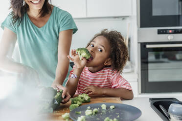 Mädchen kocht mit Mutter in der Küche und probiert Brokkoli - ERRF01667