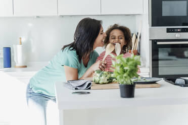 Mutter und Tochter kochen gemeinsam in der Küche und spielen mit Holzlöffeln - ERRF01668