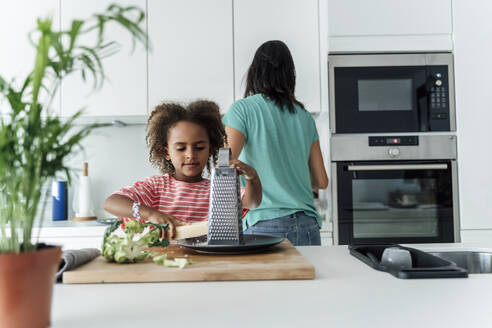 Mädchen kocht mit Mutter in der Küche und reibt Käse - ERRF01680