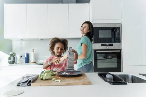 Mädchen kocht mit Mutter in der Küche und reibt Käse - ERRF01681