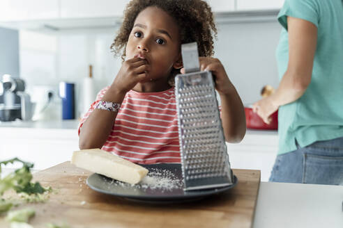 Mädchen kocht mit Mutter in der Küche und probiert geriebenen Käse - ERRF01682