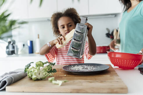 Mädchen kocht mit Mutter in der Küche und reibt Käse - ERRF01684