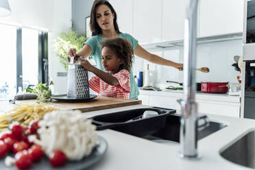 Mutter und Tochter kochen gemeinsam in der Küche und reiben Käse - ERRF01686