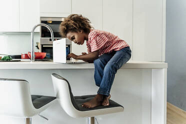 Mädchen sitzt auf dem Küchentisch und benutzt einen Laptop - ERRF01704