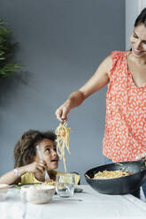 Mother serving pasta meal for daughter sitting at dining table - ERRF01717