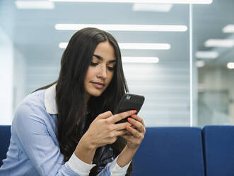 Mixed race businesswoman using cell phone in office lobby - BLEF12199