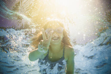 Kaukasisches Mädchen schwimmt unter Wasser und gestikuliert das Friedenszeichen - BLEF12206