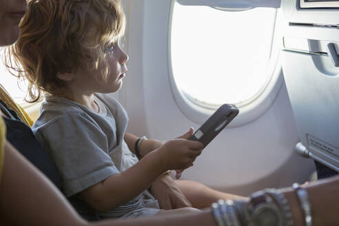 Kaukasische Mutter und ihr kleiner Sohn benutzen ein Mobiltelefon im Flugzeug - BLEF12221