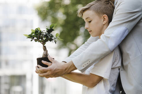 Man and boy holding bonsai tree - KMKF01014