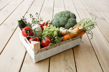 Wooden box of organic vegetables on wooden floor - KMKF01018