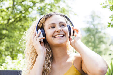 Lächelnde Frau beim Musikhören im Freien - TCF06173