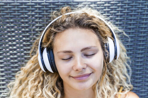 Lächelnde Frau, die mit geschlossenen Augen Musik hört, auf einem Liegestuhl liegend - TCF06180