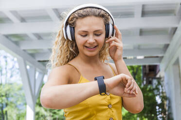 Smiling woman listening to music and looking on smartwatch - TCF06185