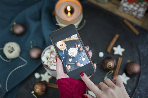 Frauenhand, die mit einem Smartphone eine Tasse heiße Schokolade mit Marshmellows fotografiert - JUNF01699