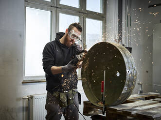 Mann bearbeitet einen Metallbehälter mit einer Schleifmaschine - CVF01354
