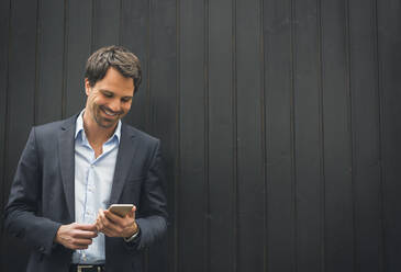 Smiling businessman looking at mobile phone - JUNF01705