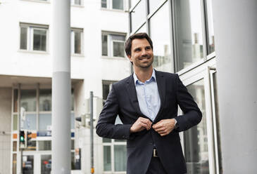 Portrait of smiling businessman buttoning his suit coat - JUNF01709