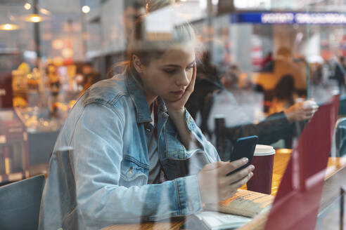 Junge Frau in einem Café, die ein Smartphone benutzt - WPEF01624