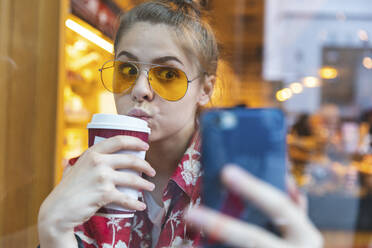 Junge Frau in einem Café, die ein Selfie macht, während sie einen Kaffee trinkt - WPEF01630